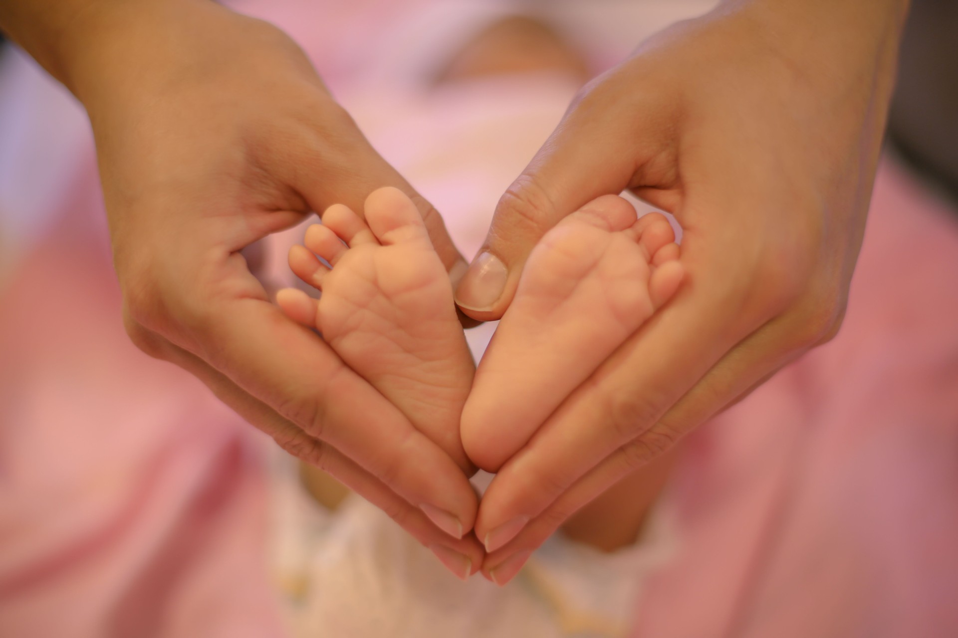 Newborn baby feet in its mother's hands shaped like a heart. Mother showing her love and affection.