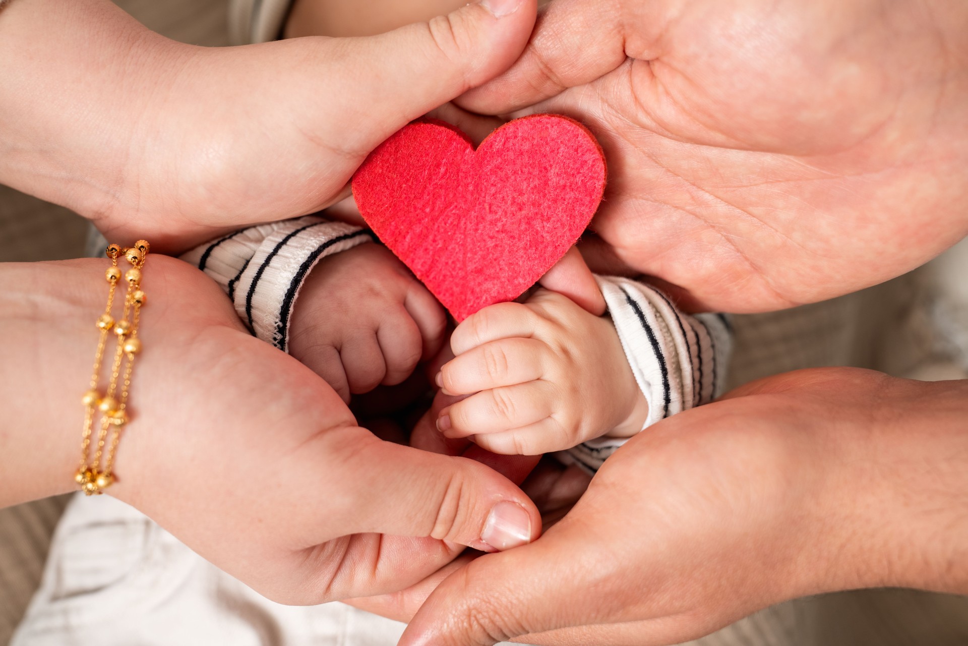 Hands of a newborn child and her parents with red heart shape