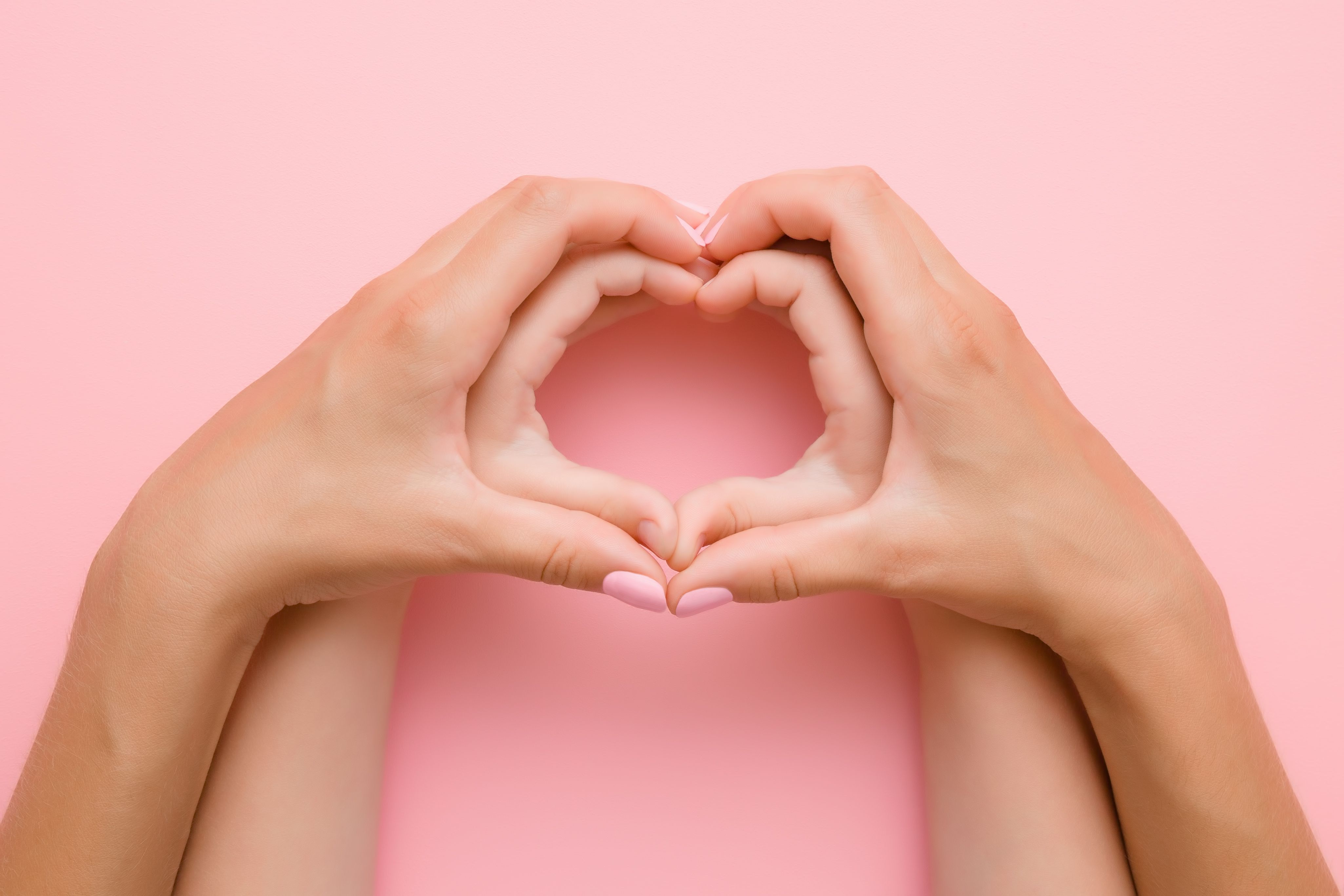 Heart shape from hands on pink background.