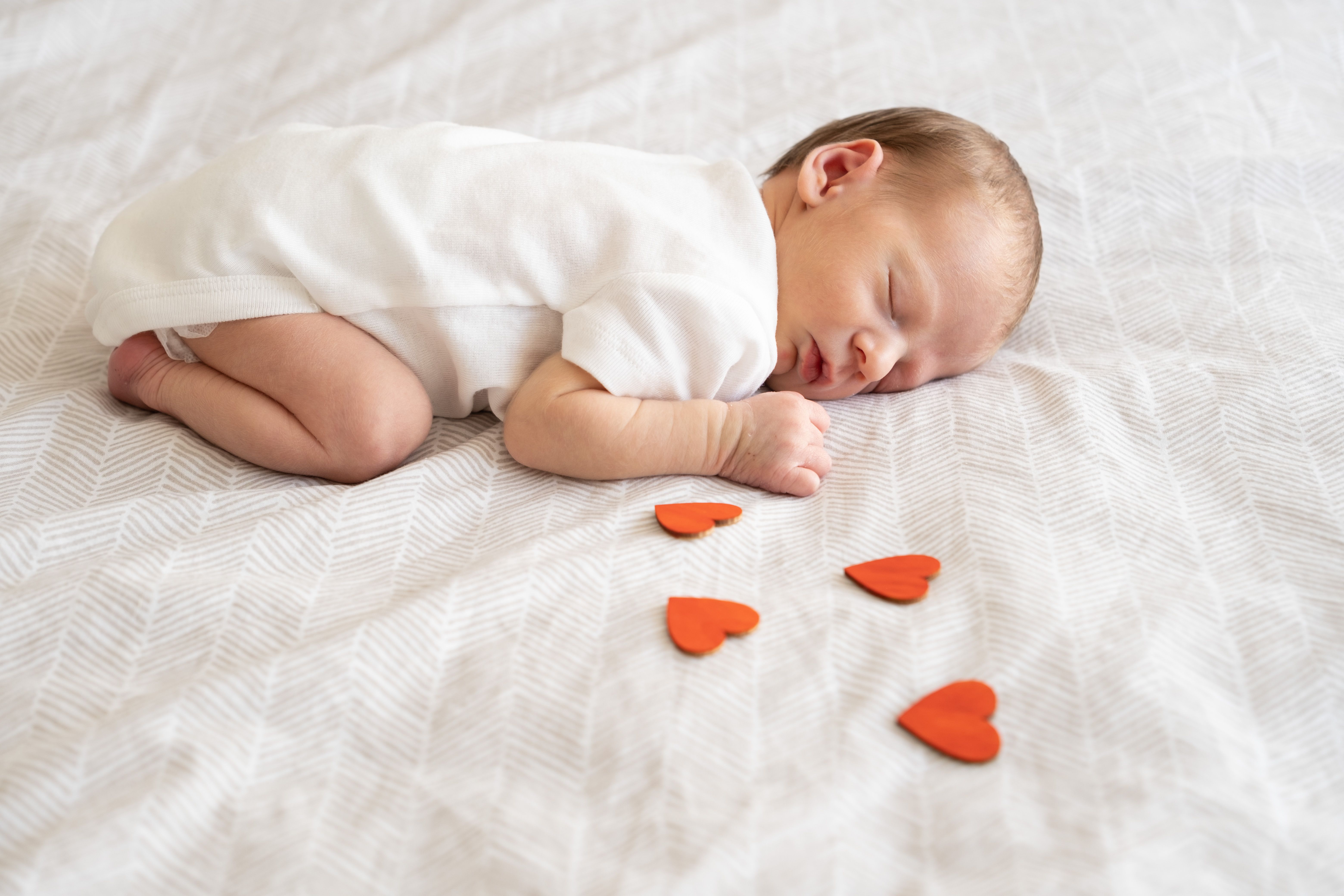 Newborn baby sleeping near wooden hearts.